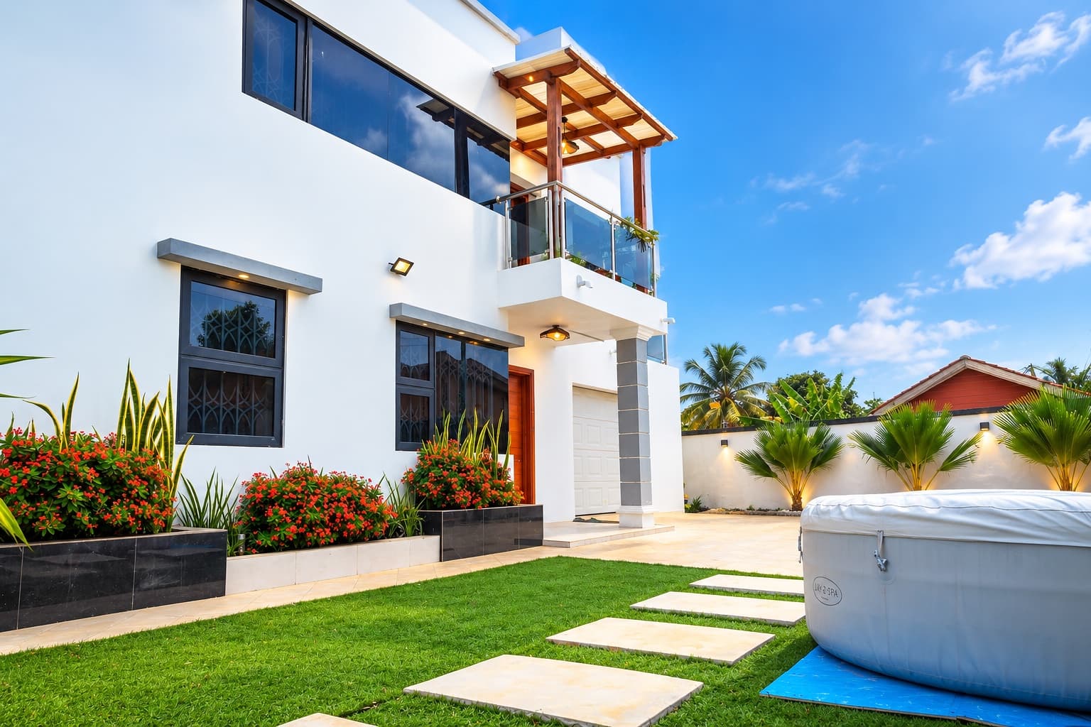 Baobab Nook from its garden, a white residence with a timber pergola balcony, flowering planters and a lawn crossed by stepping stones