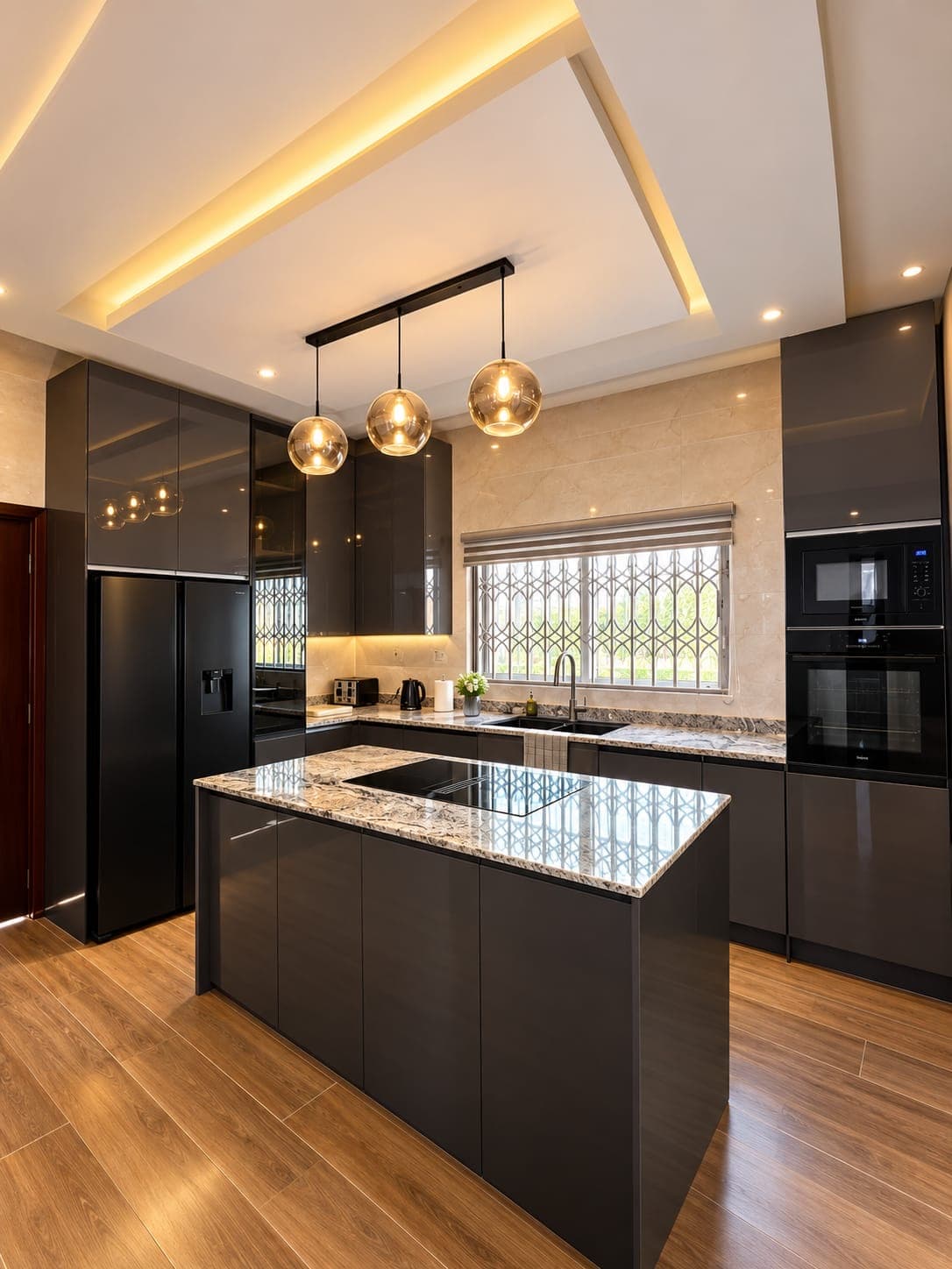 A modern kitchen with charcoal gloss cabinets, a granite-topped island with induction hob, three glass pendant lights and built-in ovens